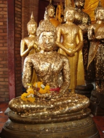Lidé lepí zlaté lístky na sošky Buddhů.