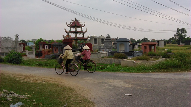 Ženy na kolech v typických kónických kloboucích míjí místní hřbitov. Projedeme se taky po okolí vesnice na kolech.